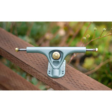 Paris V3 180mm 50º longboard truck in crystal blue with gold hardware, displayed on a wooden railing outdoors. - Longboards USA